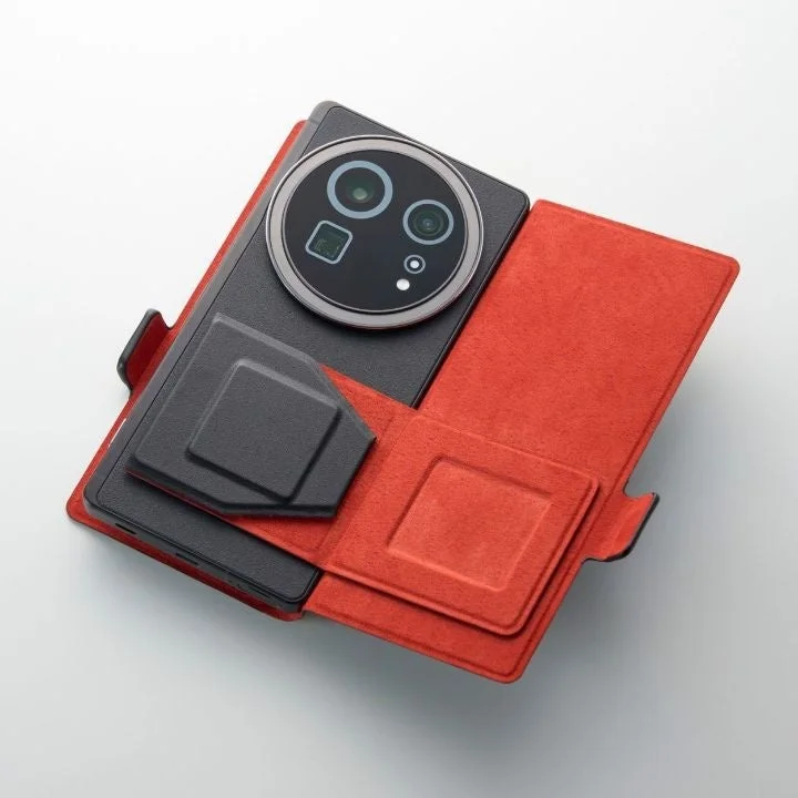 大きな円形カメラモジュールを持つ黒いスマートフォンが、開いた状態の赤いフリップ型ケースに収められています