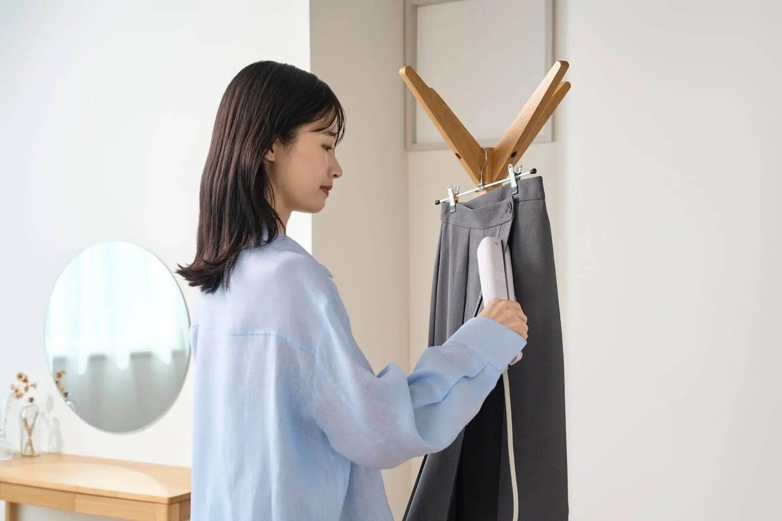 女性が自宅で衣類スチーマーを使い、グレーのパンツのシワを伸ばしている