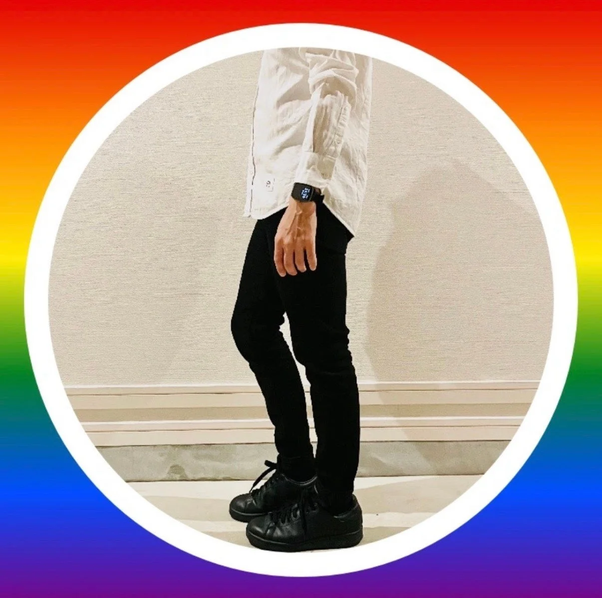白いシャツと黒いスキニーパンツ、黒いスニーカーを着用した人物の全身が写っています。左手首にはスマートウォッチがあり、背景は虹色のグラデーションで囲まれています。