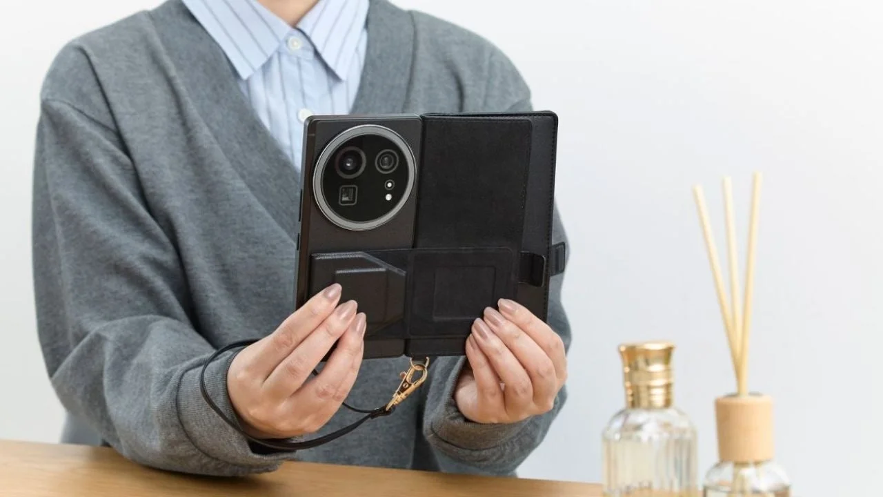 女性が大きなカメラモジュールを持つ黒いスマートフォンを、ストラップ付きのフォリオケースに入れた状態で両手で持っています