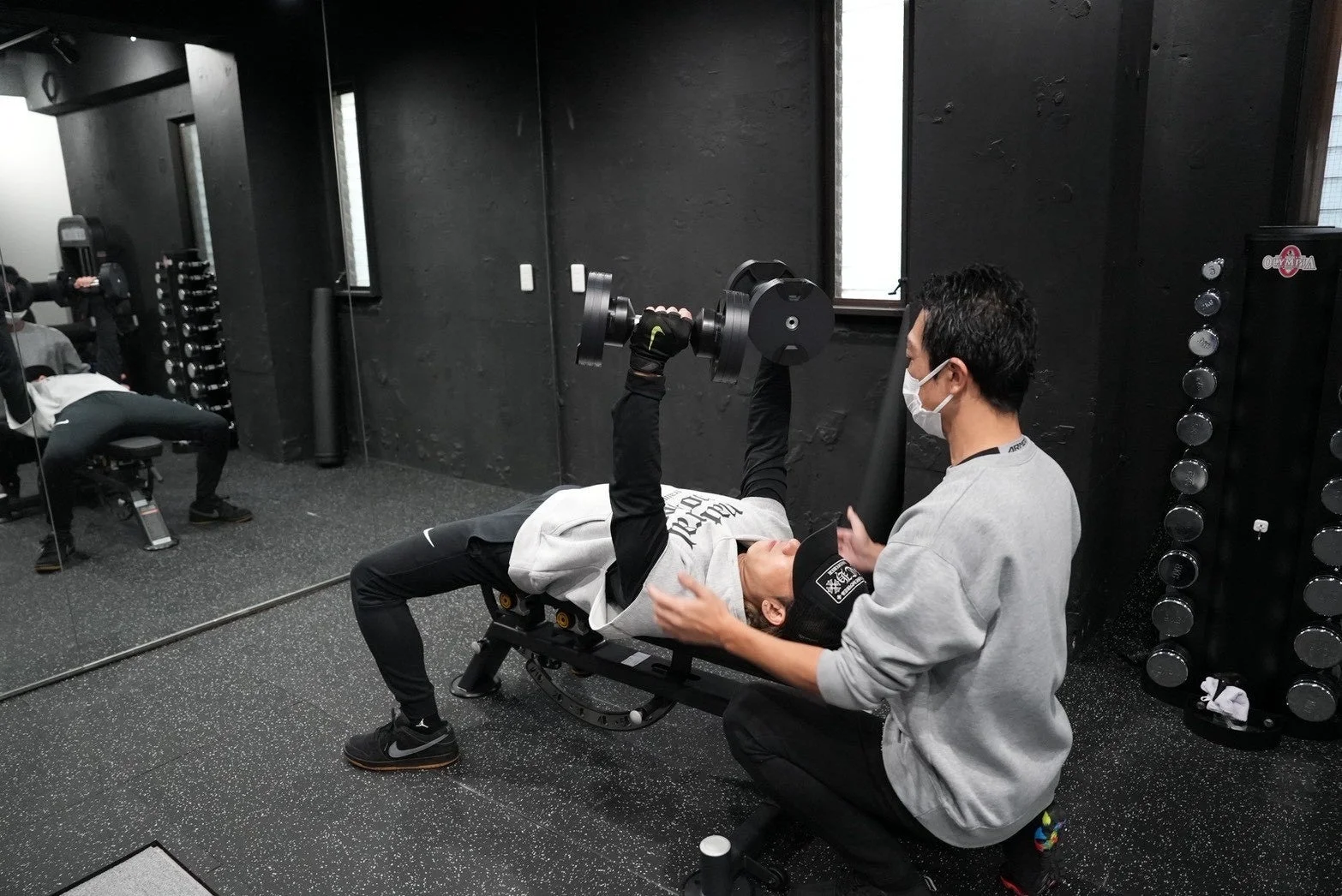 ジムでベンチプレスを行う男性と補助するトレーナー