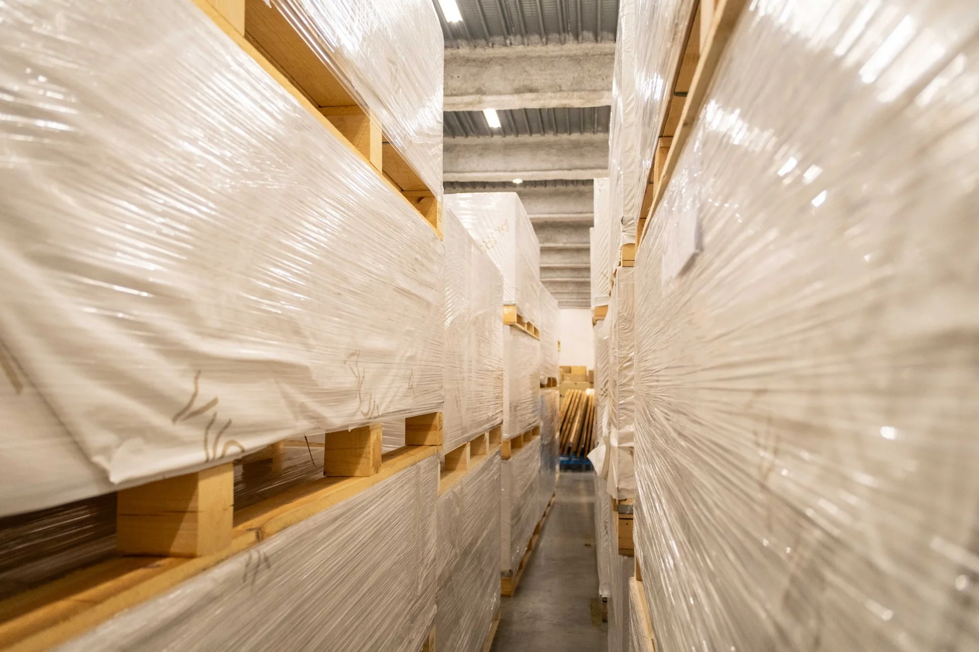 倉庫内にストレッチフィルムで包装された大量の荷物が木製パレットに積まれ、通路を挟んで整然と並べられています