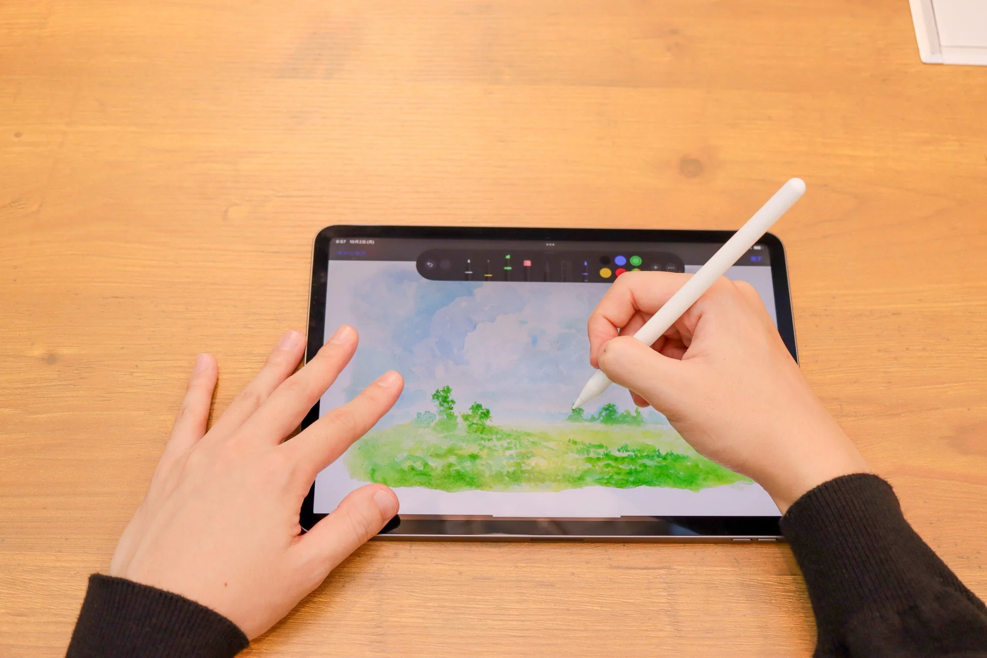 人物がタブレットとスタイラスペンを使い、水彩画のような緑豊かな風景を描いている様子