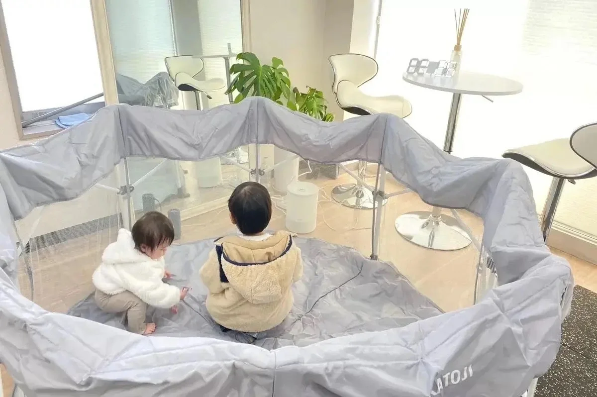 明るいリビングルームのような空間で、2人の幼い子供がKATOJI製のプレイヤードの中で遊んでいる様子