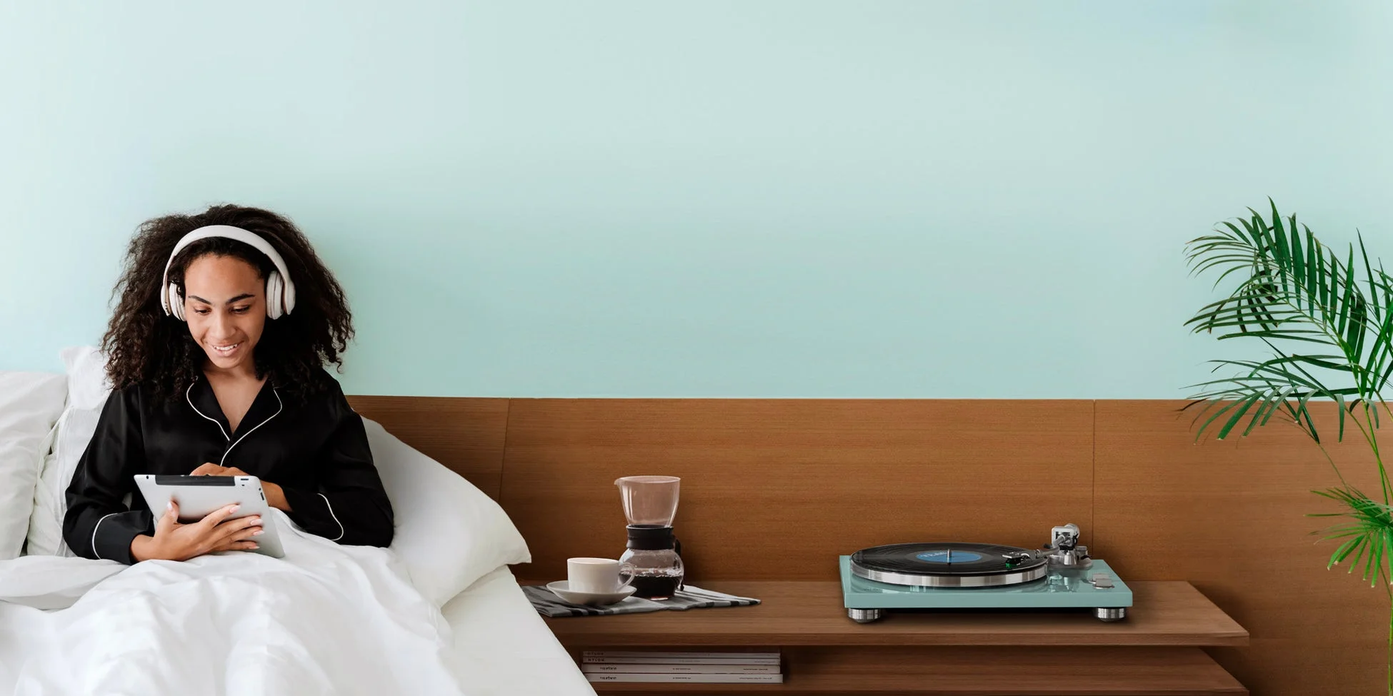 ベッドの上でヘッドホンをつけタブレットを操作する女性、隣にレコードプレーヤー