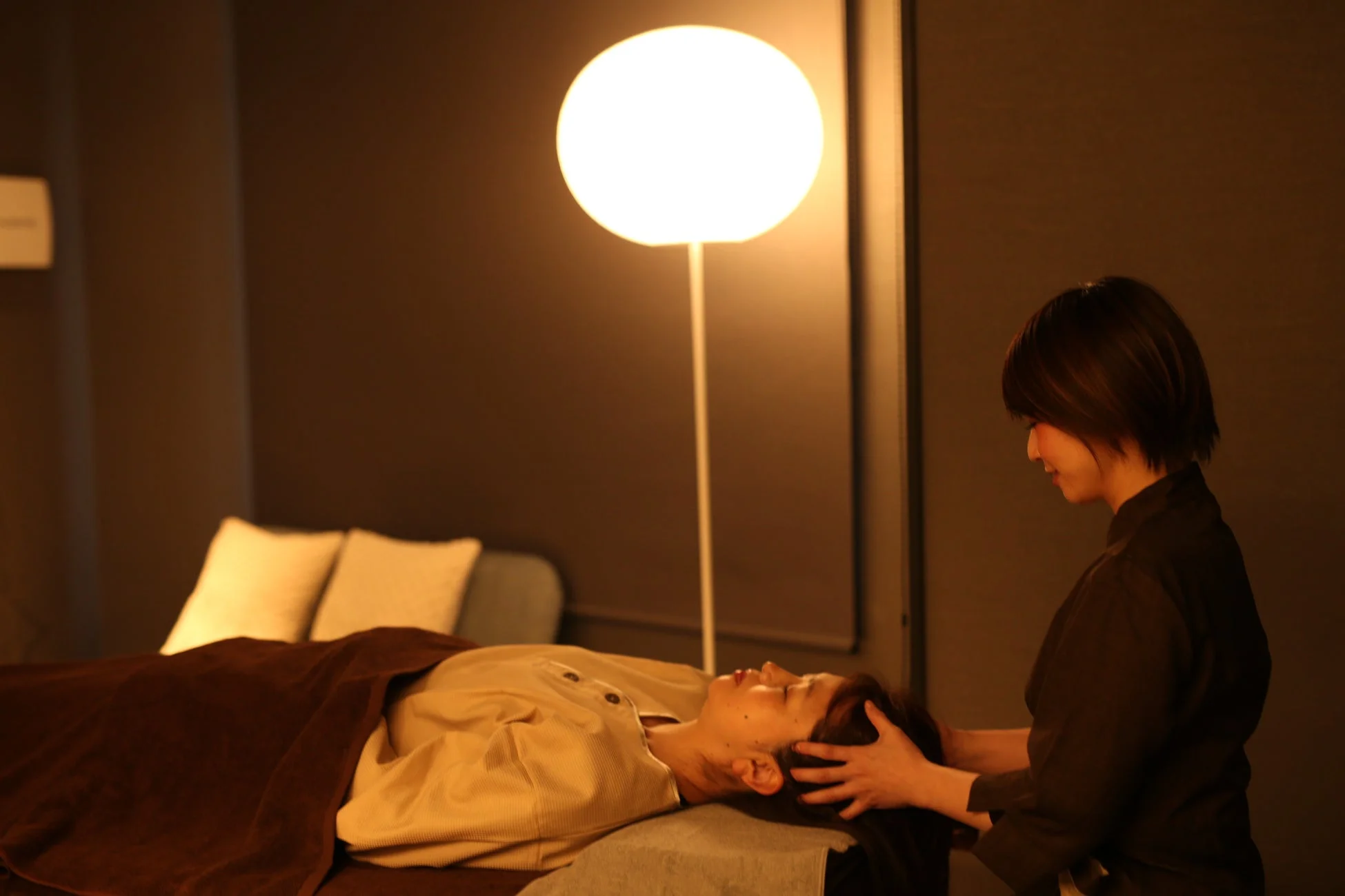 落ち着いた照明のリラックスできる空間でヘッドマッサージを受ける女性