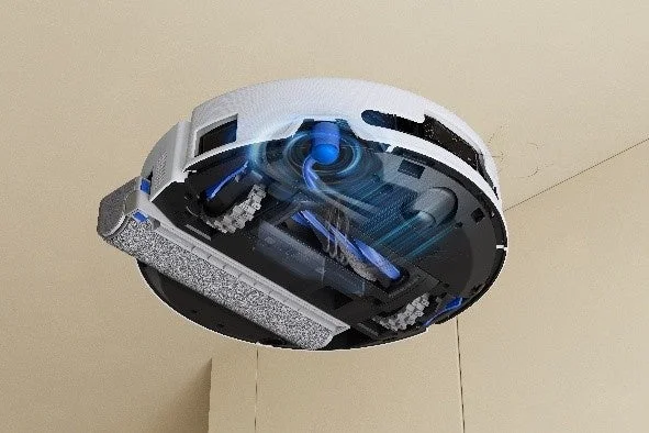 白いロボット掃除機の底面が映し出されており、内部の吸引ファン、ブラシ、ローラーなどの清掃メカニズムが青い光と線で強調されています。機能的な構造を示すイメージです。