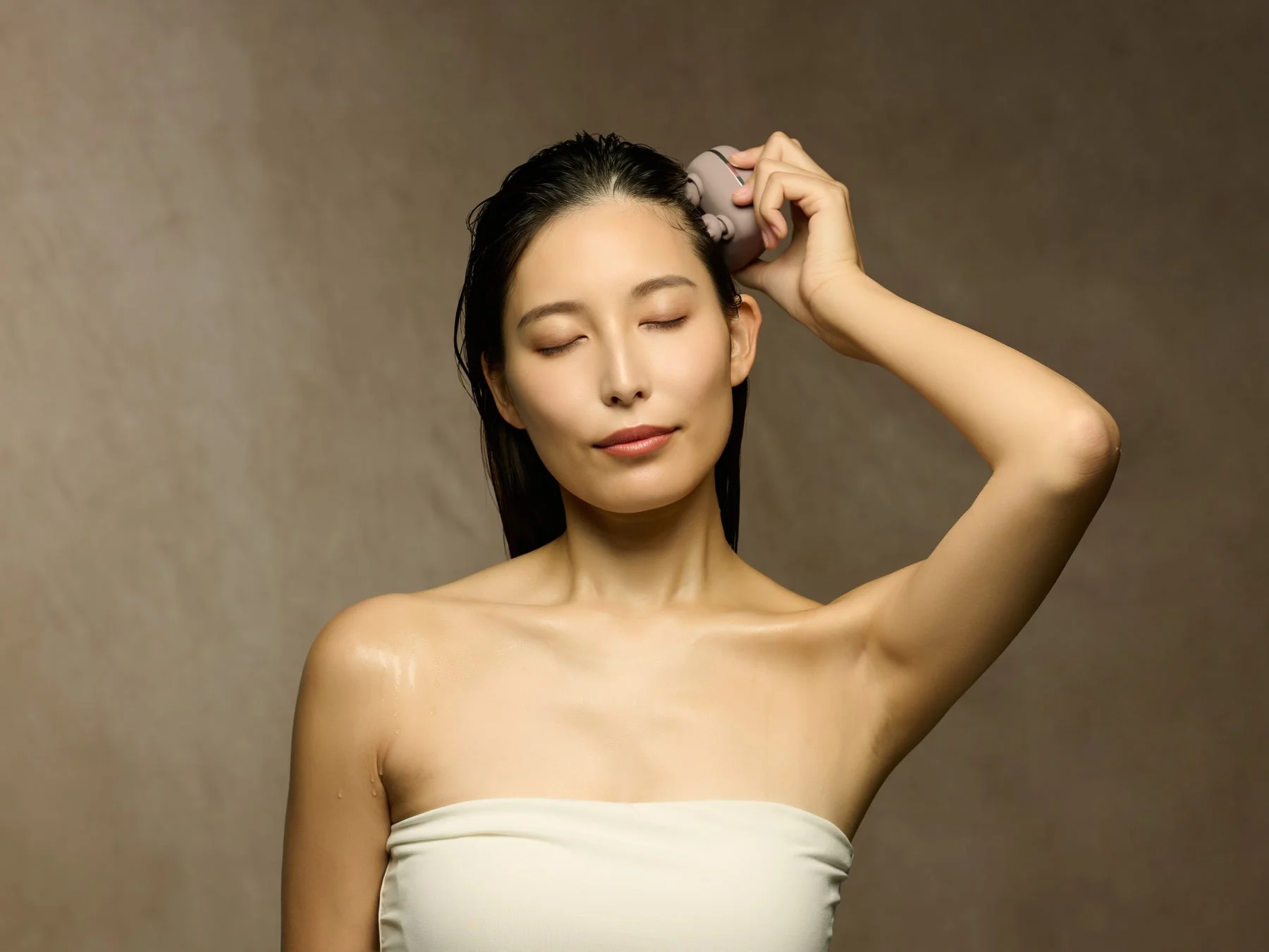 女性がヘッドマッサージャーで頭皮ケアをする様子