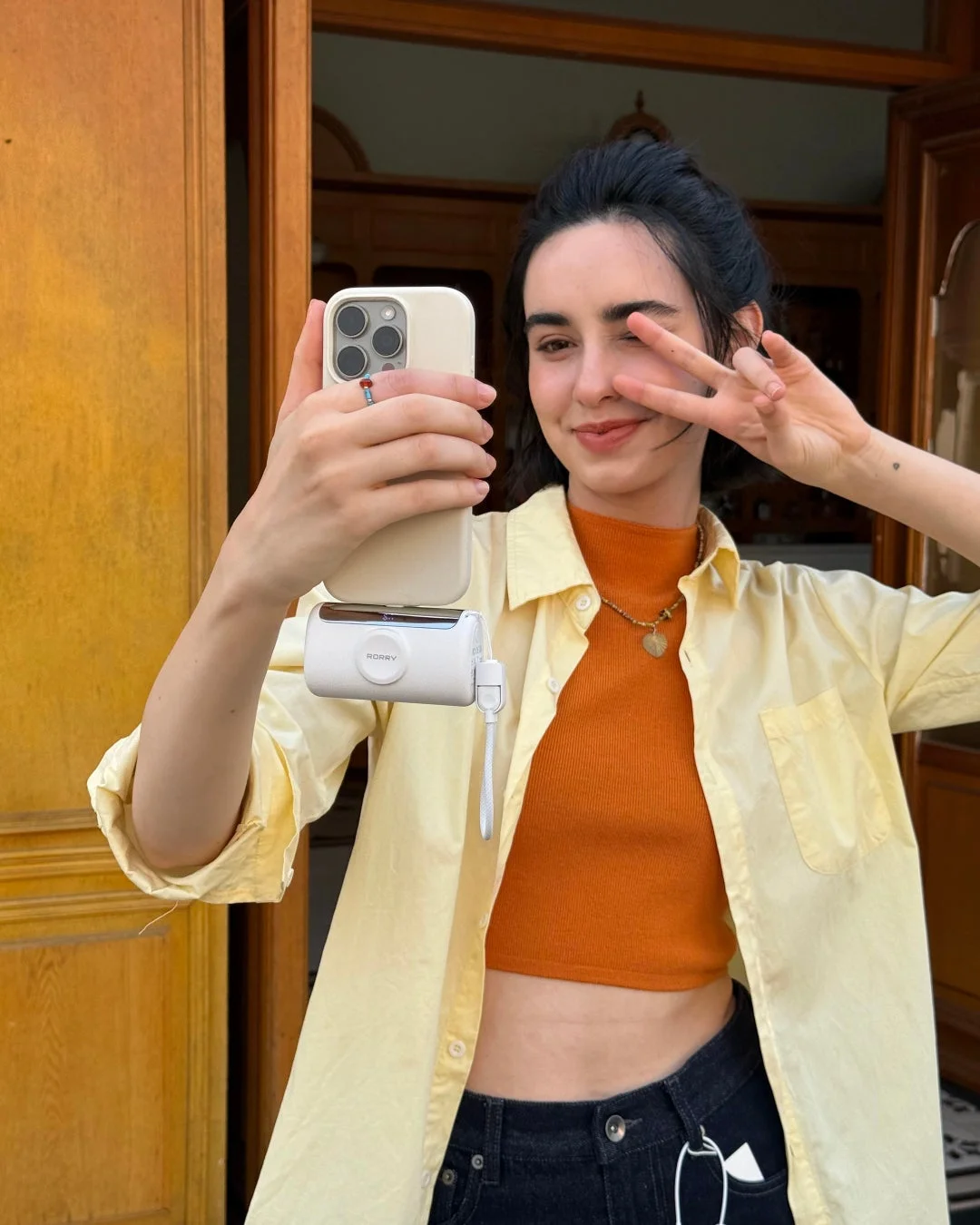 女性がスマートフォンとモバイルバッテリーを持ってピースサインをしている様子