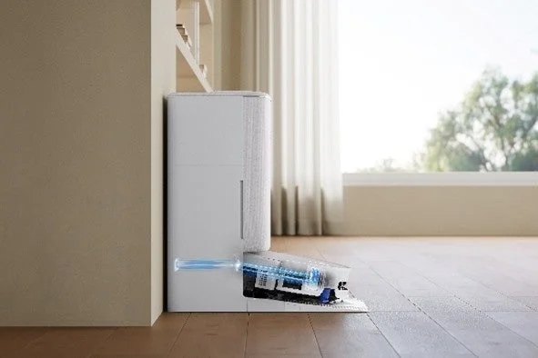 ロボット掃除機がドッキングステーションから出て、フローリングの部屋を掃除している様子。明るい窓から光が差し込むモダンなリビング空間で、スマート家電が活躍している場面を捉えています。