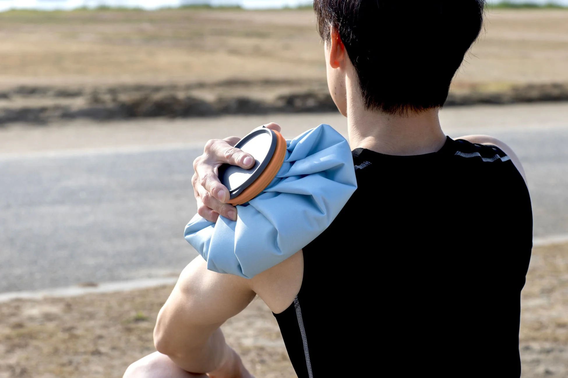 屋外で肩にアイスバッグを当てる男性