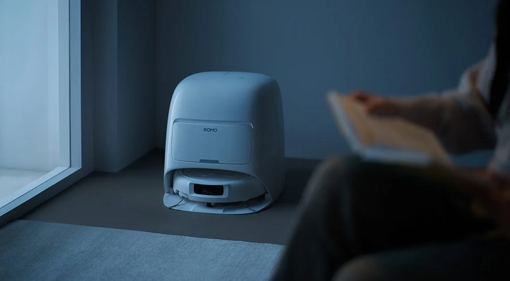 薄暗い室内に設置された自動ゴミ収集機能付きロボット掃除機「ROMO」