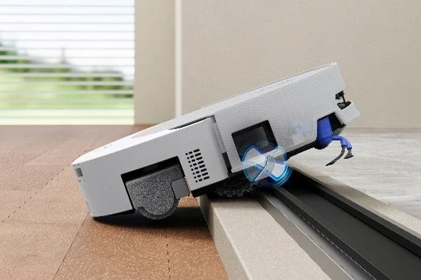 フローリングから別の床材への段差を乗り越えるロボット掃除機の様子。自動で床を清掃し、異なる床面間の移動もスムーズに行える機能を示している。