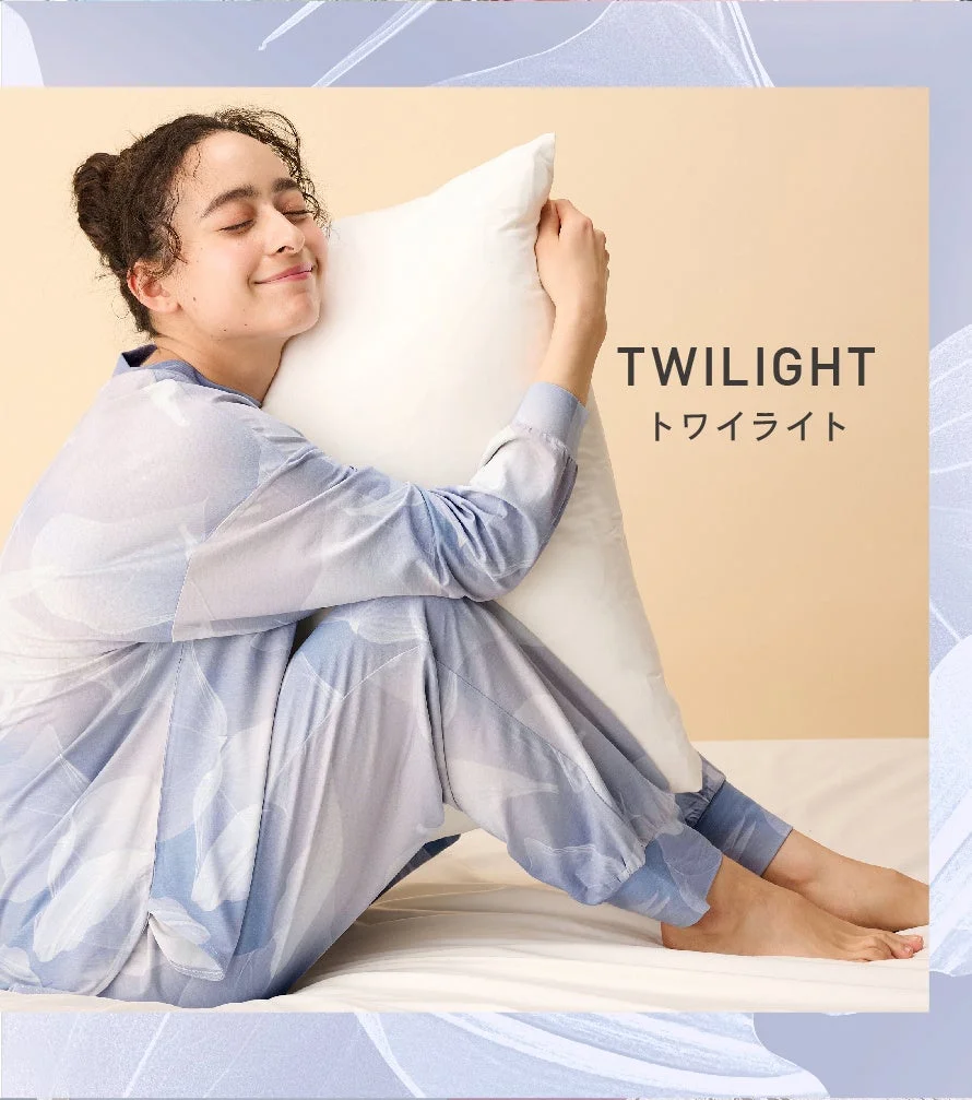 青いパジャマを着た女性が白い枕を抱きしめ、幸せそうな笑顔を見せています。