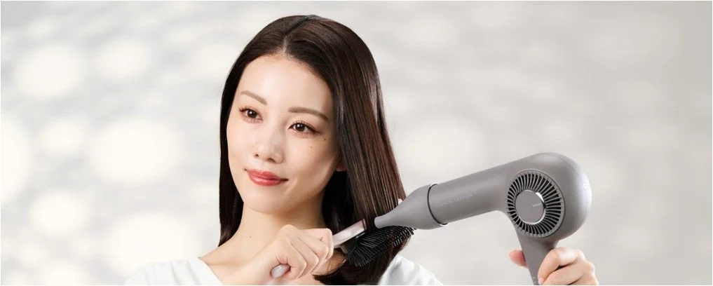 ヘアドライヤーとブラシで髪をブローする女性