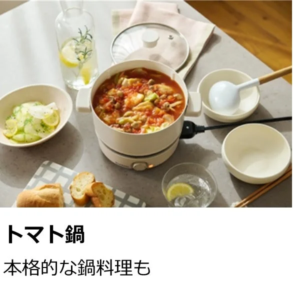 テーブルに置かれた電気鍋でトマト鍋が調理されており、きゅうりのサラダやパン、飲み物などが並べられた食卓の様子です。