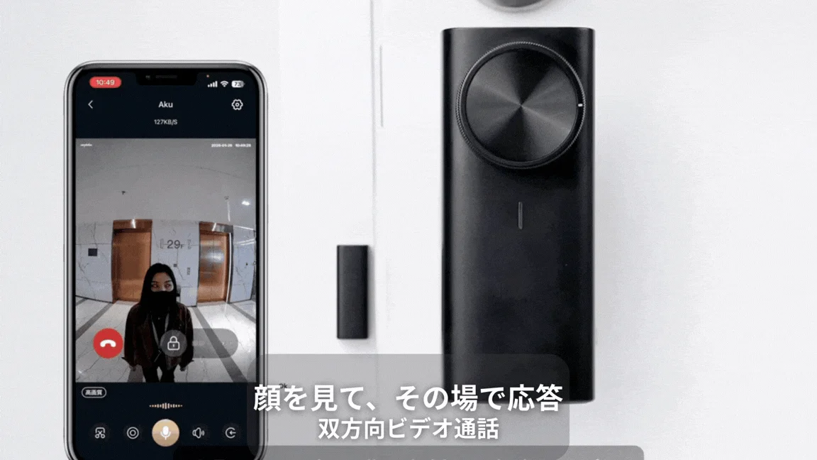 スマートフォンにスマートドアベルアプリの画面が表示されており、エレベーターホールにいる人物との双方向ビデオ通話の様子が映し出されています