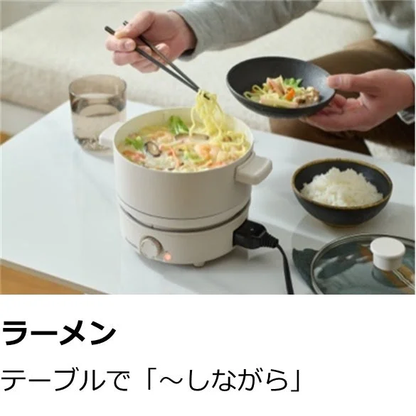 食卓に置かれた電気鍋で調理されたラーメンを、箸で取り分けている様子を捉えた画像です。