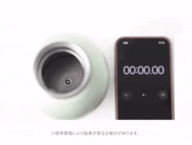 ライトグリーンの機器からミストが噴霧されており、隣にはストップウォッチが00:00.00を表示するスマートフォンが置かれている。製品の機能テストの様子で、「※使用環境により結果が異なる場合があります」との注意書きがある。
