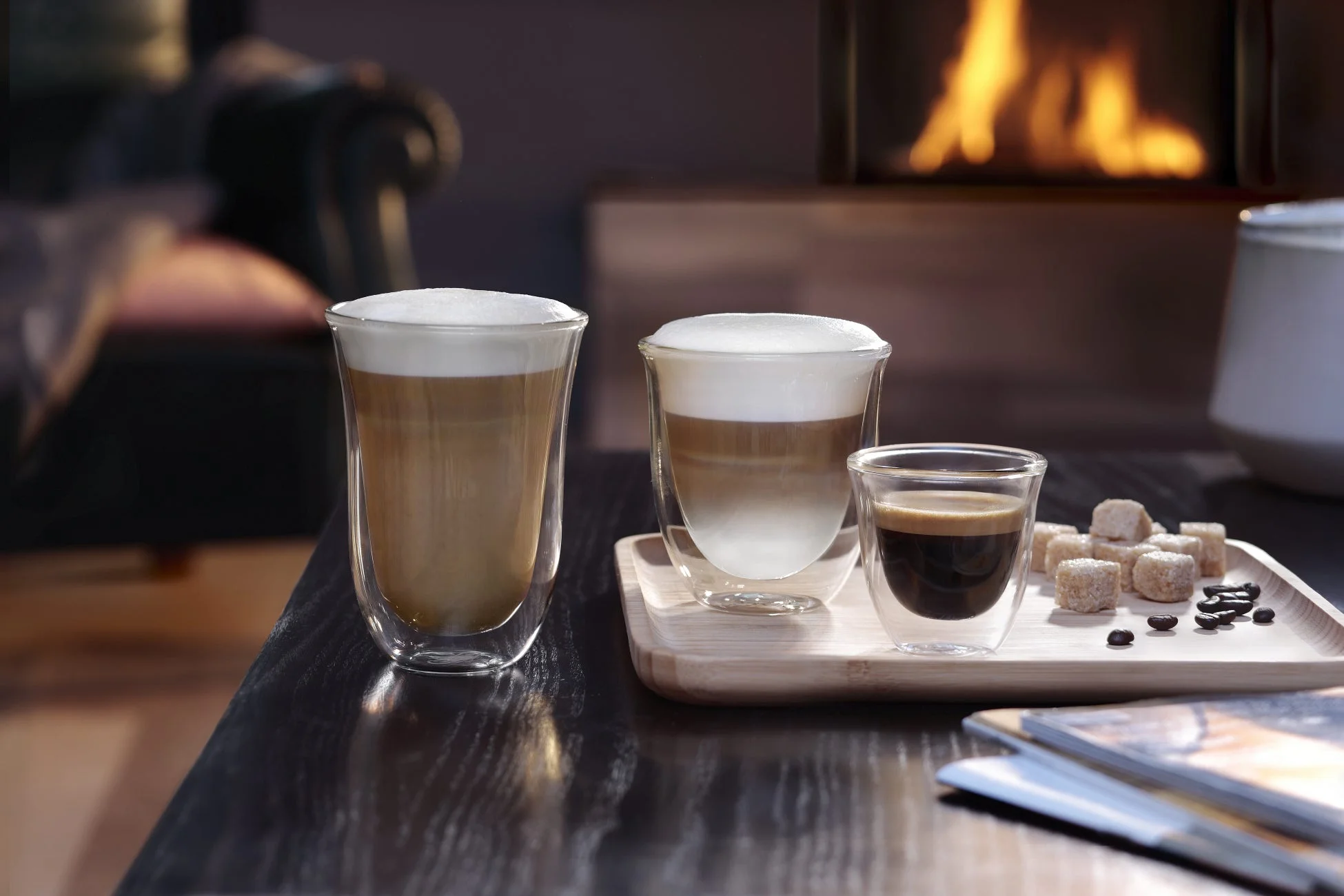 暖炉の温かい火を背景に、カフェラテ、ラテマキアート、エスプレッソの3種類のコーヒーが並べられています