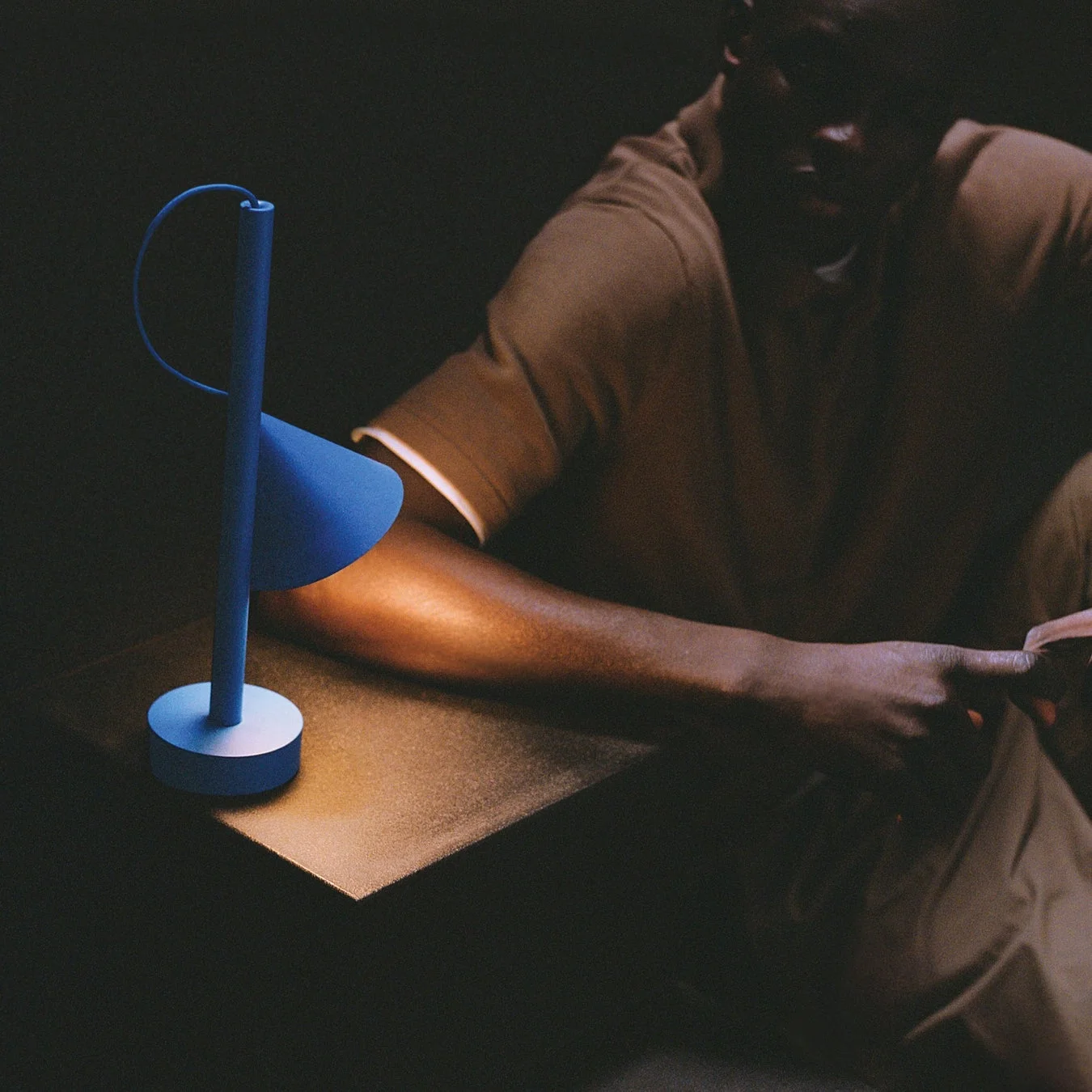 青いモダンなデスクランプが置かれた部屋で人物が光の下にいる様子