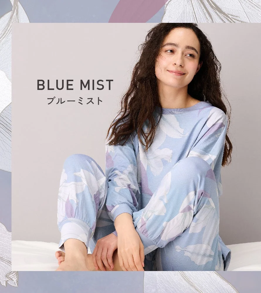 青い花柄のパジャマを着た女性が笑顔で座っている画像です。