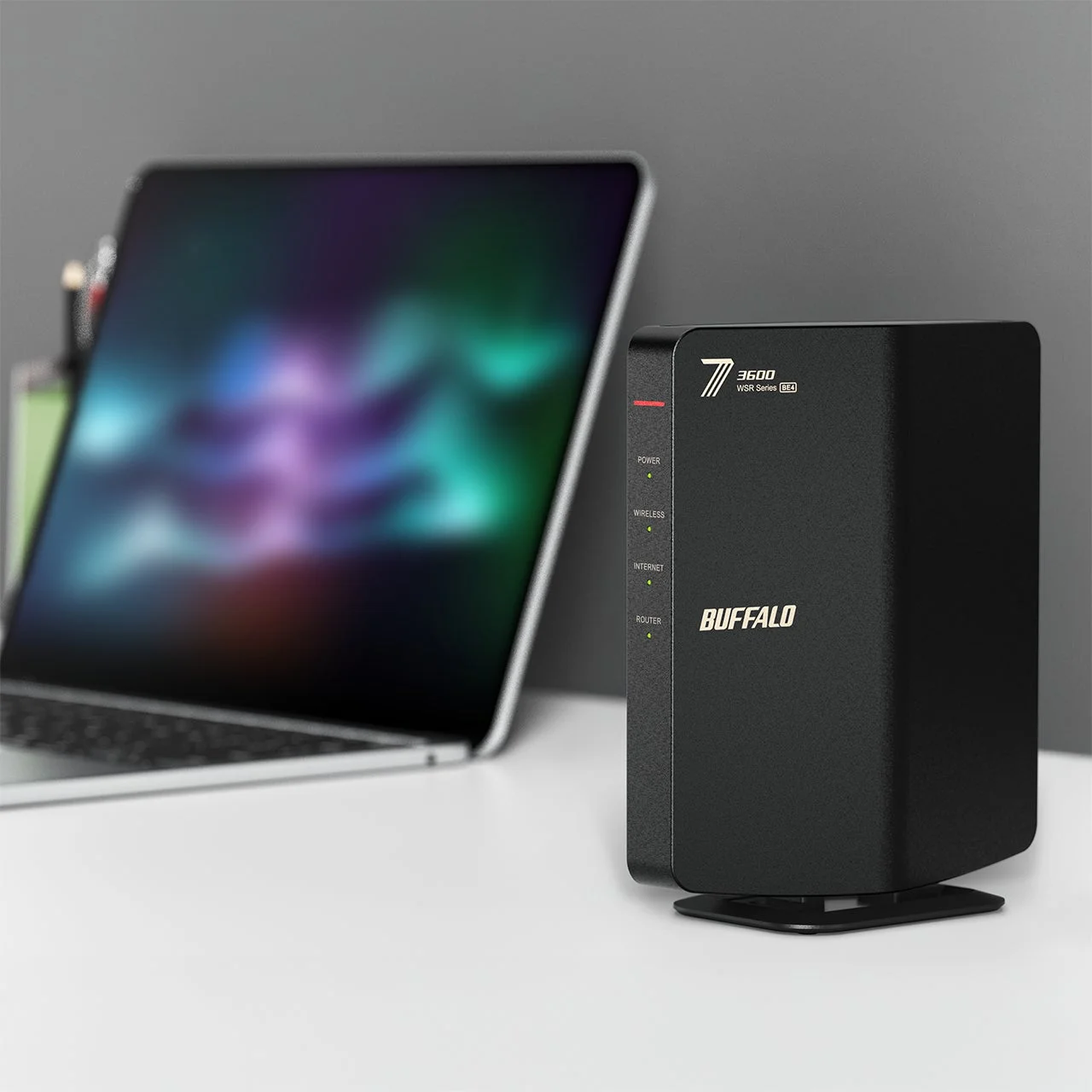 白いデスクに置かれた黒いWi-FiルーターとラップトップPC