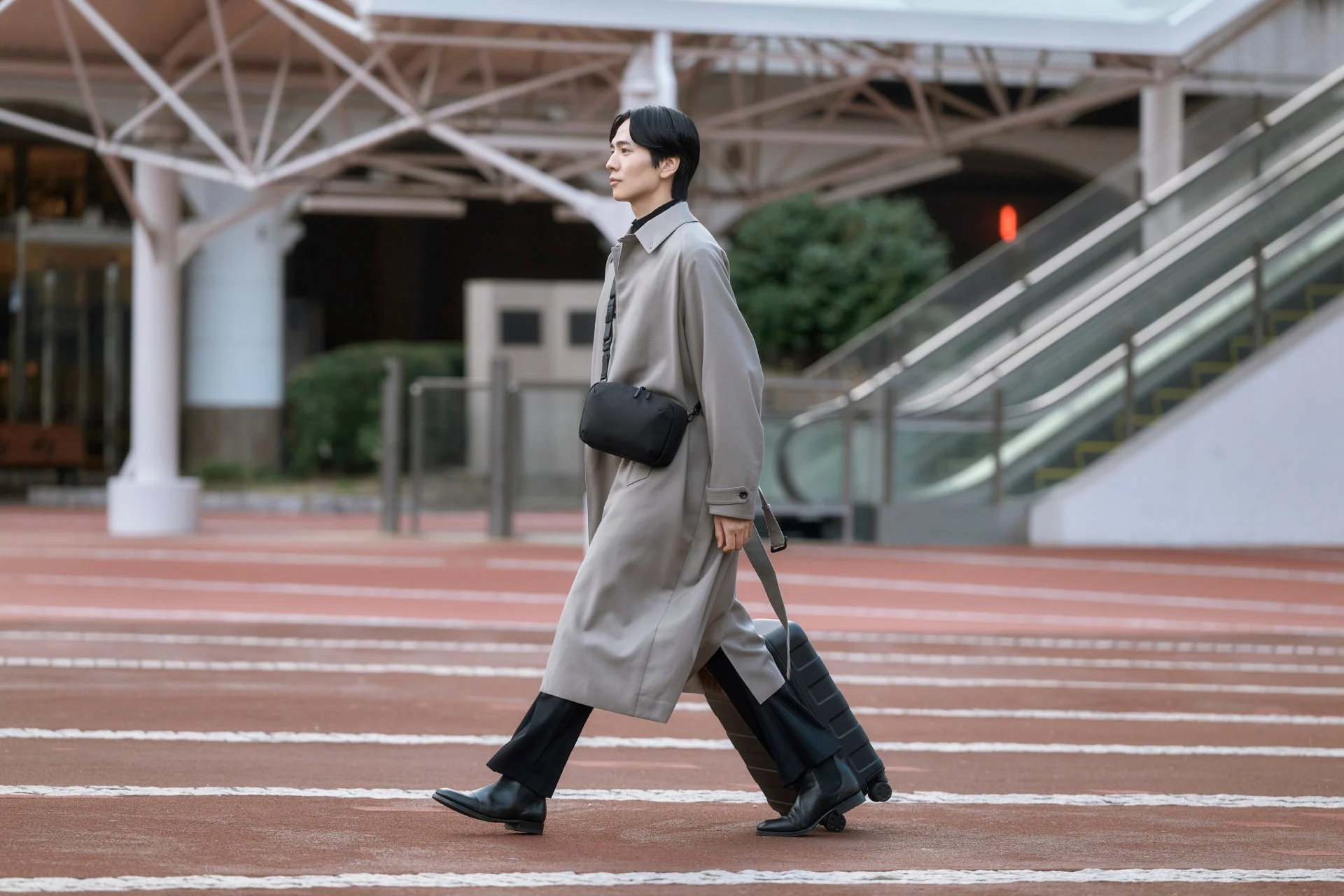 男性がショルダーバッグを身につけ、スーツケースを引いている画像