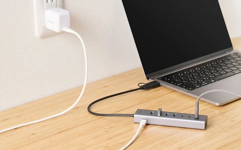 ノートパソコンが多機能USBハブに接続され、充電器から給電されている様子