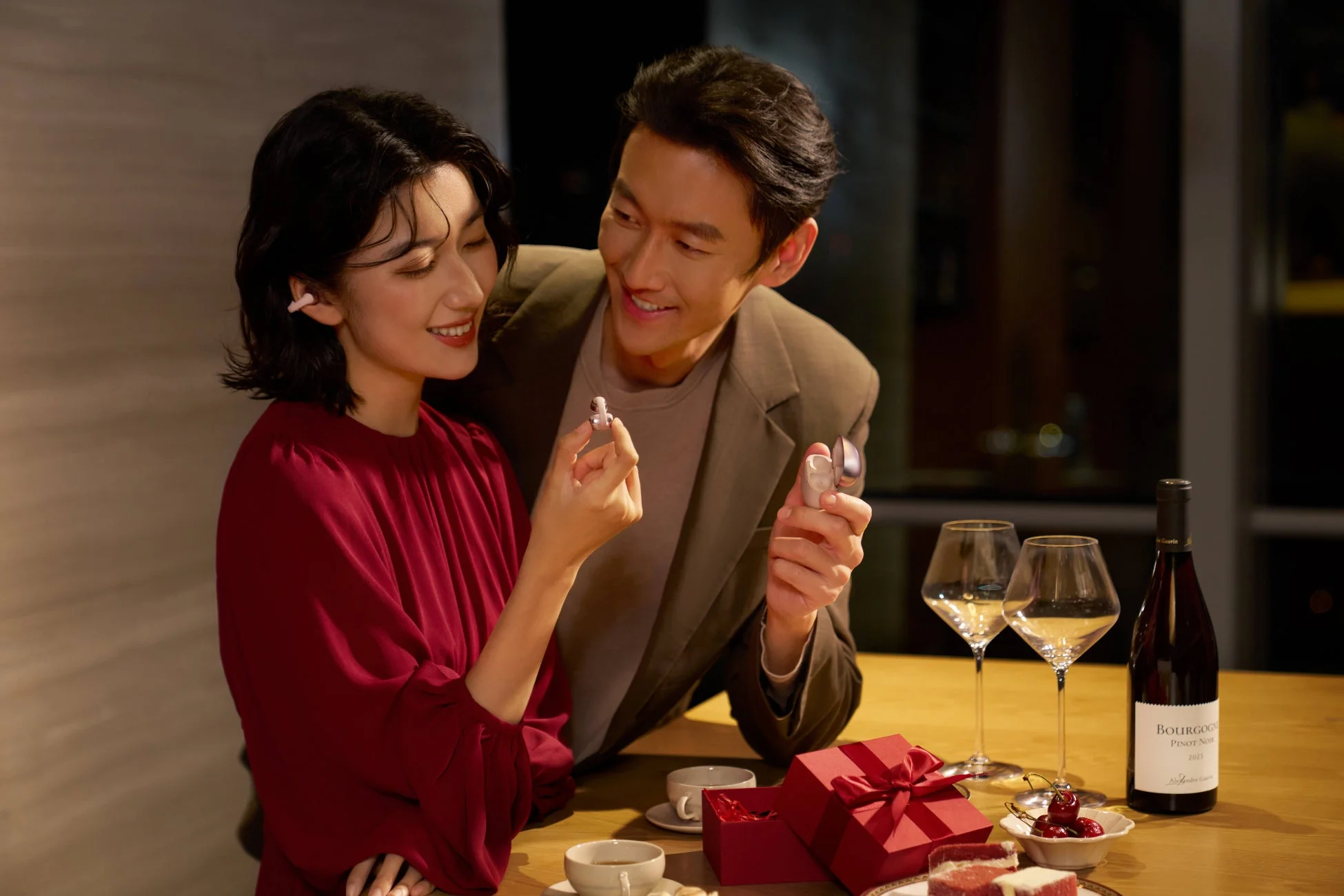 笑顔のカップルが、ワイヤレスイヤホンを見せ合いながら楽しそうに会話している画像