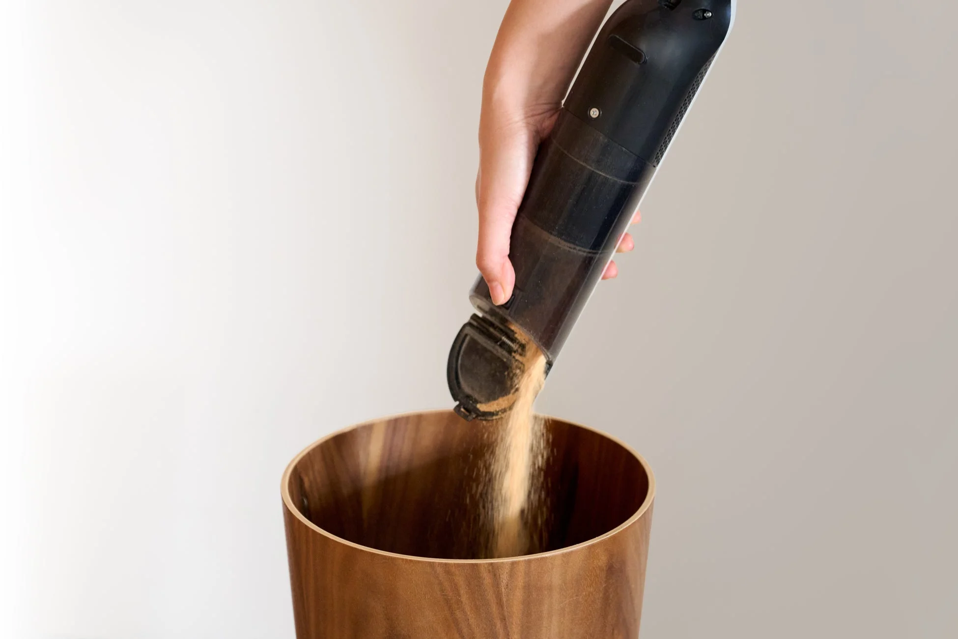 ハンディクリーナーで吸い取ったゴミを木製のゴミ箱に捨てている場面