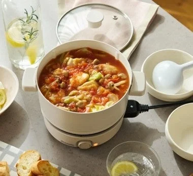 電気鍋で温かいトマトベースの煮込み料理が食卓に並べられている様子です。