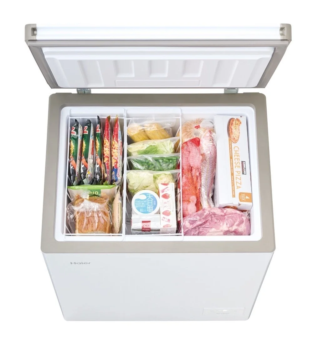 Haier製のチェストフリーザーが上から見た視点で写されており、内部には冷凍食品、肉、魚、野菜などが種類別に整理されて収納されている様子がわかる。