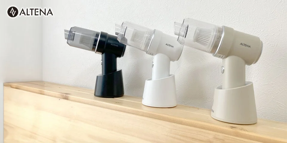 ALTENAブランドのスタイリッシュなハンディクリーナーが、黒、白、ベージュの3色で木製の台の上に並べられています。コンパクトでモダンなデザインが特徴のコードレス掃除機です。
