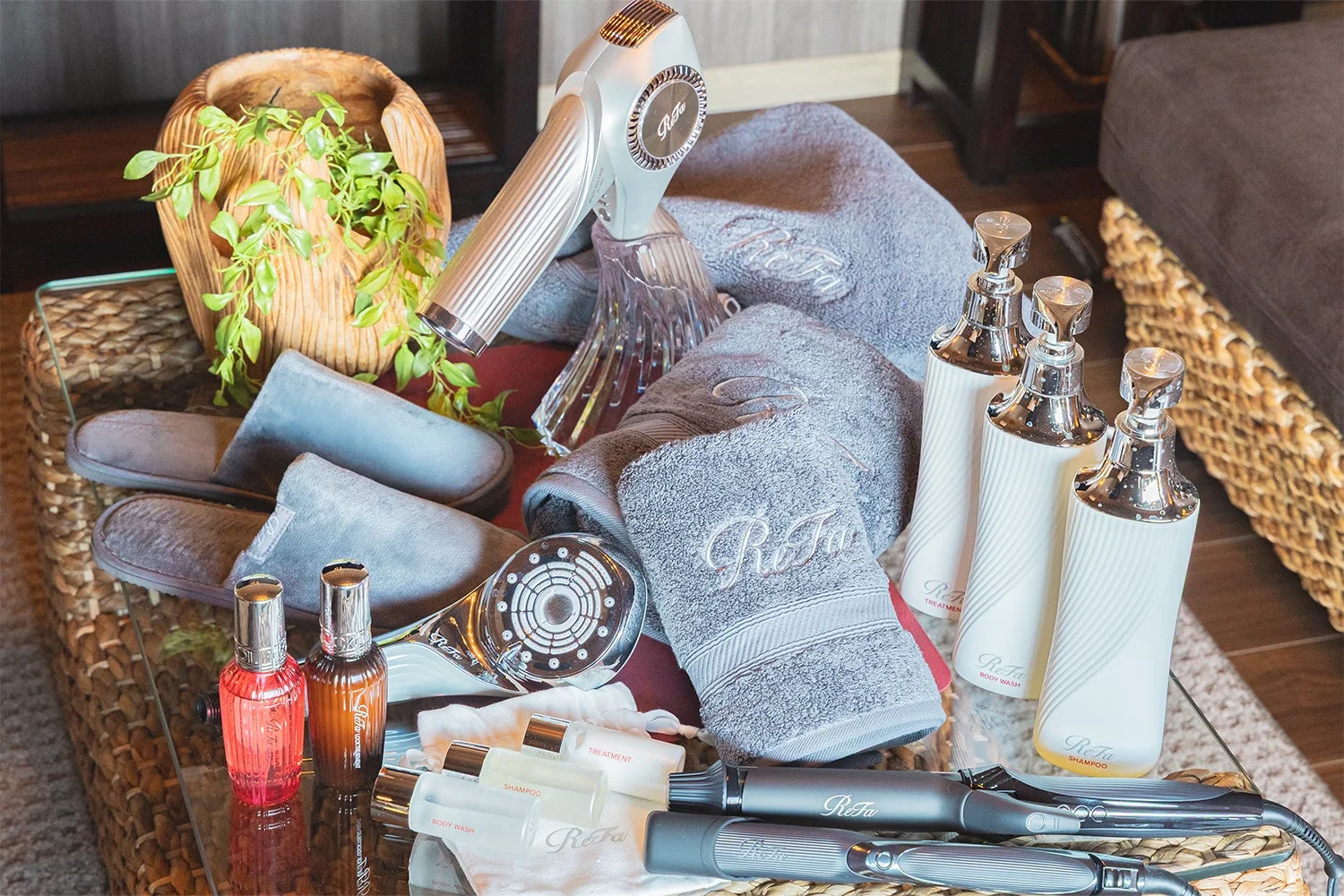 Refaブランドの美容家電（ヘアドライヤー、ヘアアイロン、シャワーヘッド）や、ロゴ入りタオル、スリッパ、シャンプー、ボディウォッシュ、トリートメントなどのアメニティが並べられた画像です。ホテルやスパの客室に用意された上質なアイテム群を示しています。