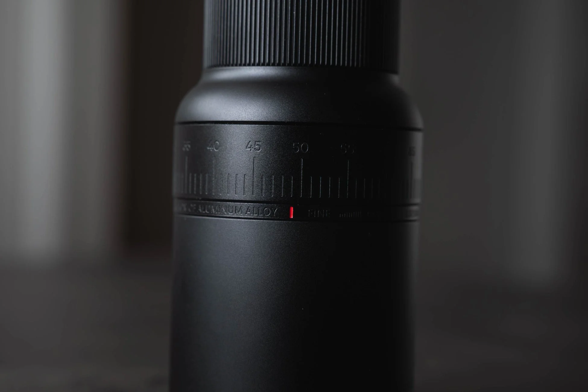 黒い円筒形の物体がクローズアップで写されており、表面には「OF ALUMINUM ALLOY」という文字と「FINE」という単語、そして「35」から「55」までの数字と目盛りが刻まれています。赤い縦線が現在の設定を示しているようです。
