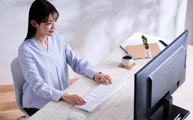 デスクでパソコンに向かい、白いキーボードを操作する女性