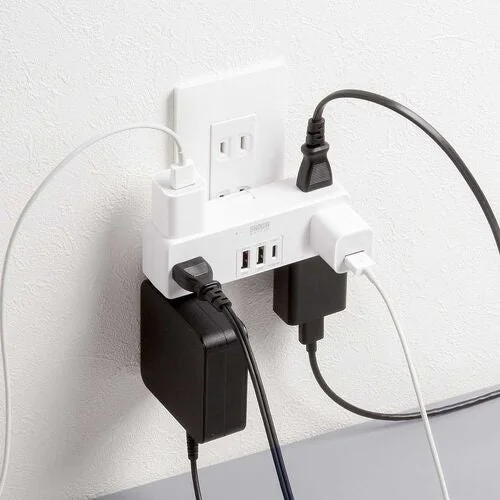 壁のコンセントに差し込まれた白い電源タップと、そこに接続された複数の充電器やケーブルが写っています。複数の機器を同時に充電・給電できる状態を示しています。