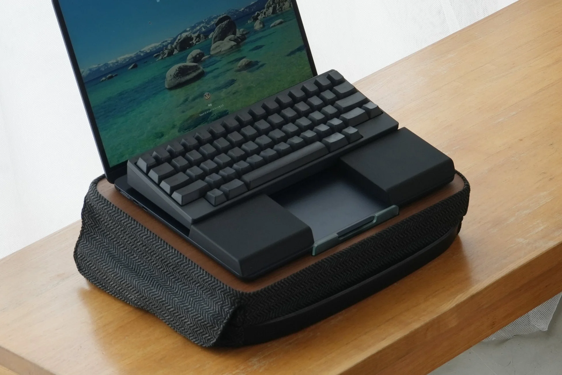 木製の机の上にノートパソコンと外付けキーボードが設置されたワークスペース。画面には湖の風景が広がり、リラックスした環境で作業ができる様子が伝わります。