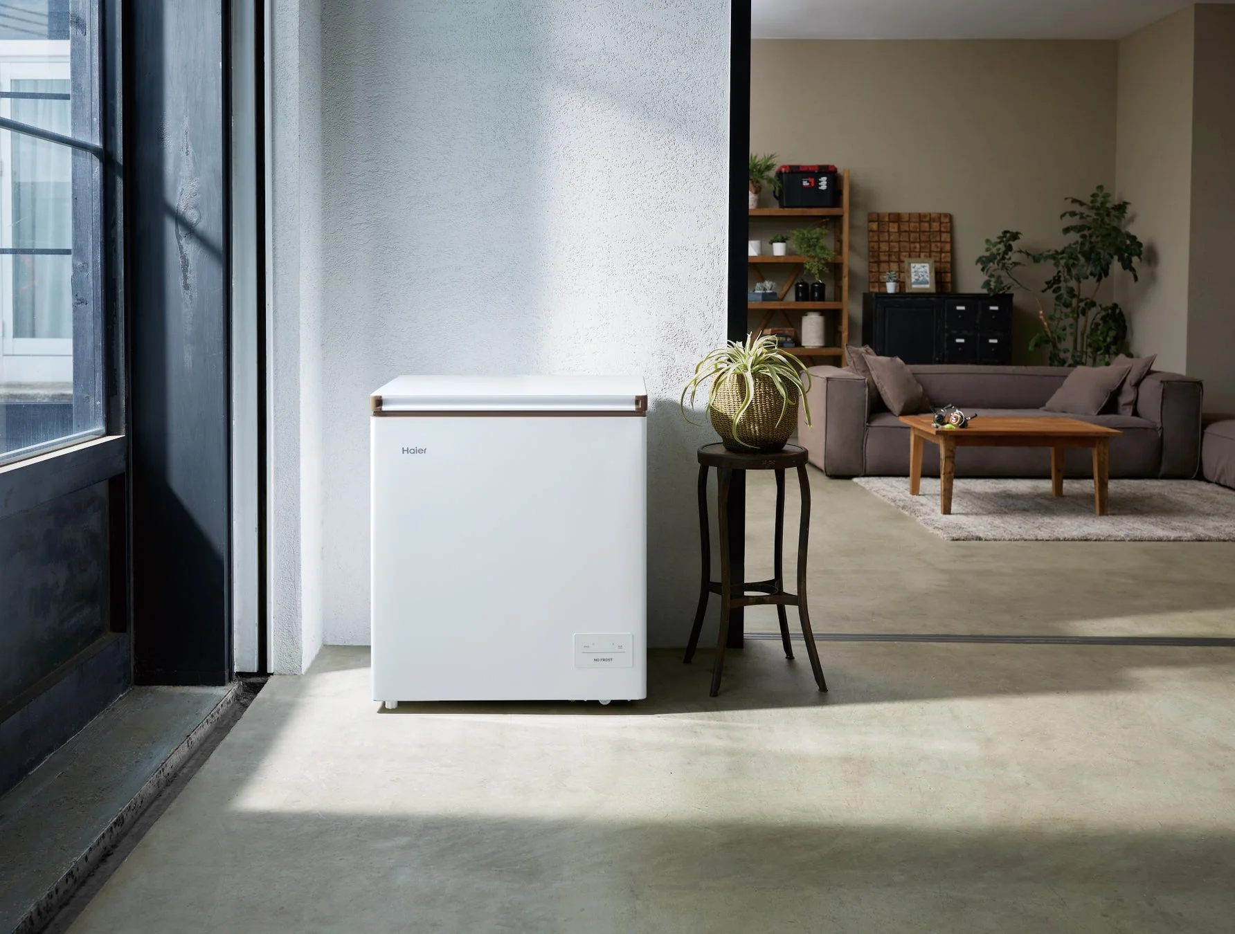 モダンなリビングの一角に白い冷凍庫が置かれています。奥にはソファや棚のあるリラックスできる空間が広がり、機能的でありながらインテリアに溶け込むデザインが特徴的です。