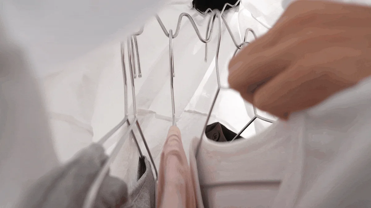 クローゼットの内部から見た視点で、手がハンガーにかかった衣類に触れている様子