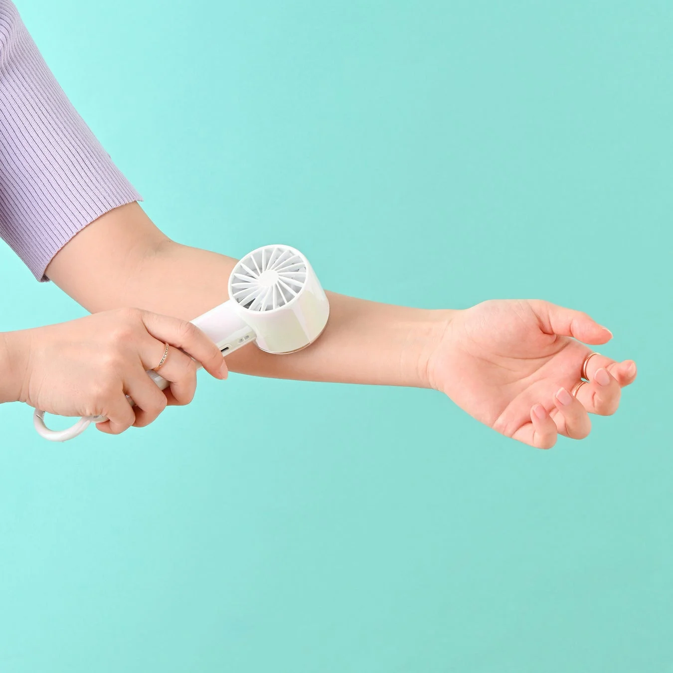 ミントグリーンの背景で、女性が白いハンディファンを腕にあてて冷却している様子