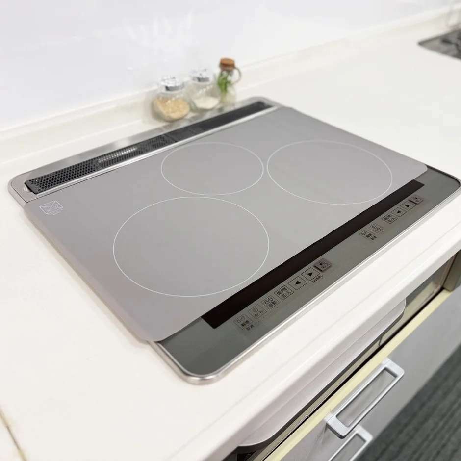 清潔感のあるモダンなキッチンに設置されたIHクッキングヒーターを捉えた画像です。複数の調理ゾーンと操作パネルが見え、奥には調味料の瓶が置かれています。機能的で整頓された調理空間の様子が伺えます。