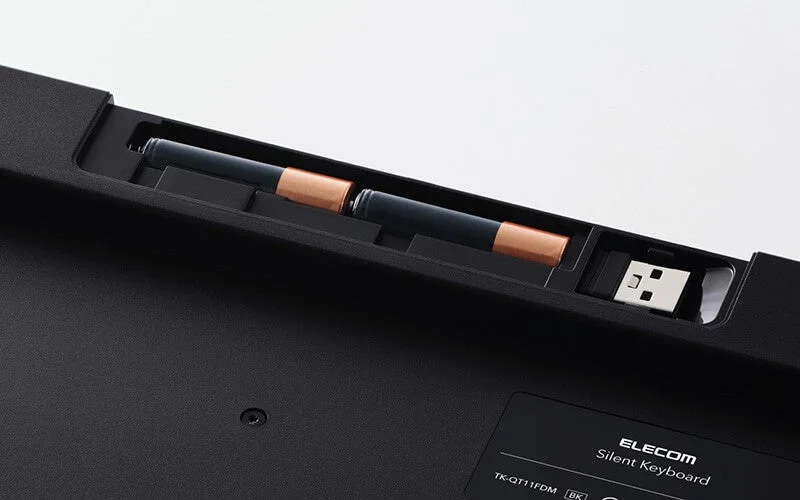 黒いワイヤレスキーボードの裏面で、単三電池2本とUSBレシーバーが収納されている様子