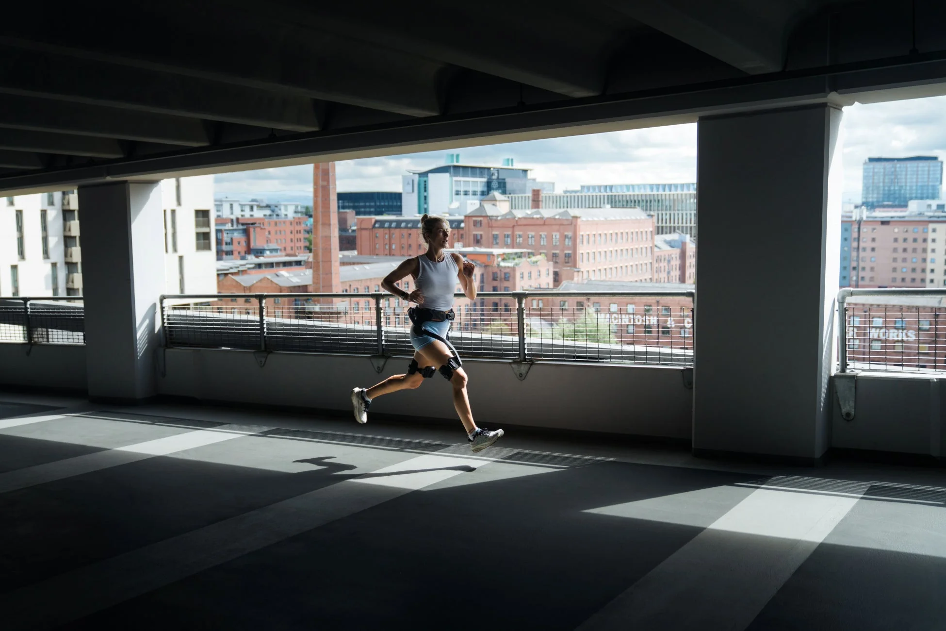 都市の建物が見える開放的な駐車場のフロアで、スポーツウェアを着た女性がランニングをしている様子