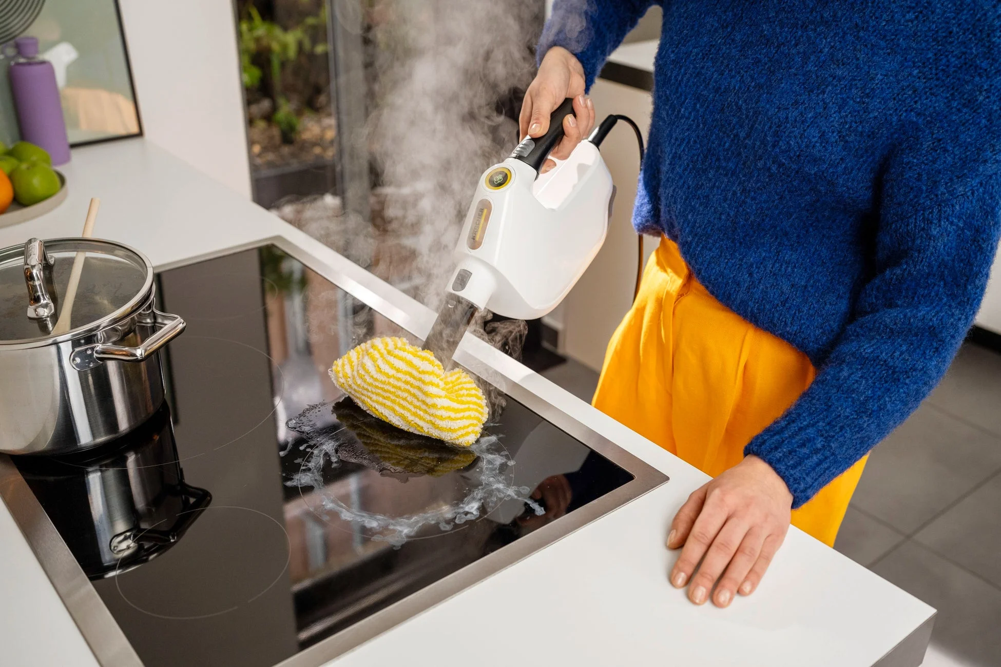 キッチンで女性がケルヒャーのスチームクリーナーを使い、IHクッキングヒーターの頑固な汚れを強力な蒸気で掃除している様子です。効率的で衛生的な清掃作業が伺えます。