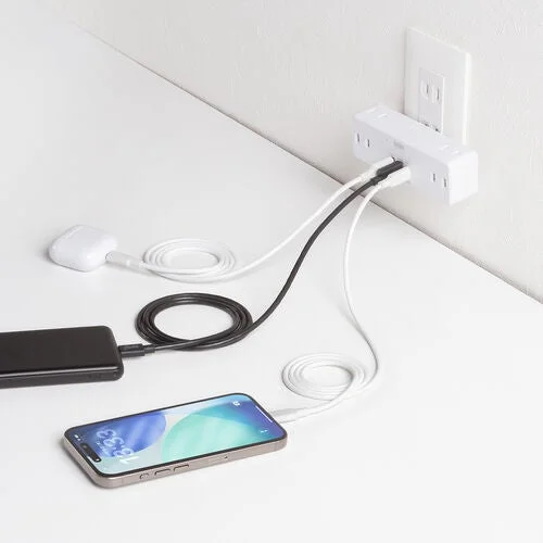 複数のデジタルガジェット（スマートフォン、モバイルバッテリー、AirPods）が、壁の電源タップに接続された充電器から同時に充電されている様子を捉えた画像です。白を基調とした清潔感のある空間で、ケーブルも整理されています。