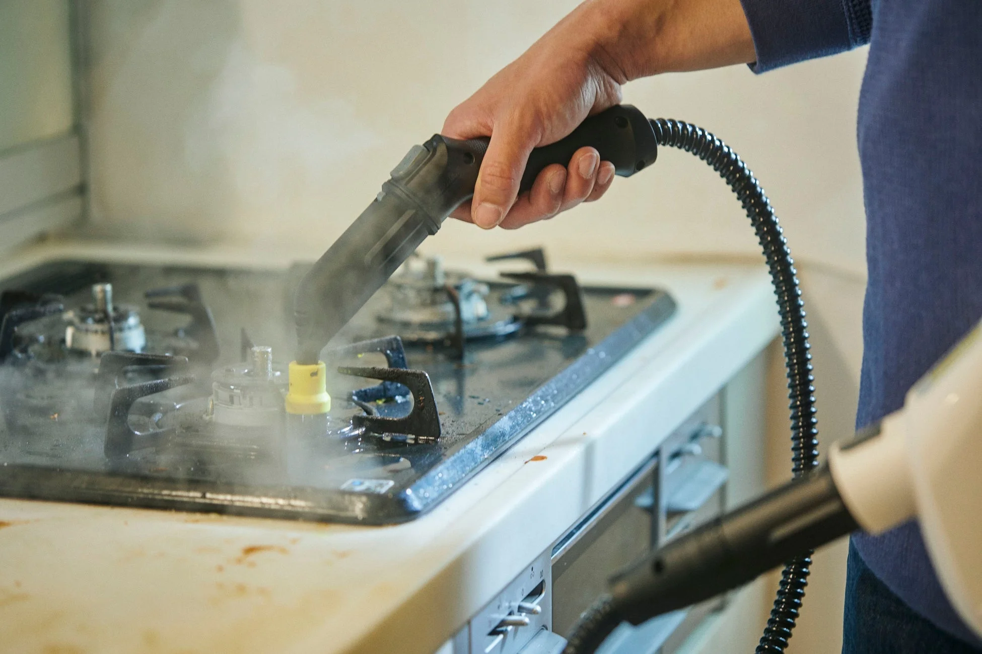 スチームクリーナーを使ってガスコンロを清掃している様子。高温の蒸気で頑固な油汚れを効果的に落としている場面です。