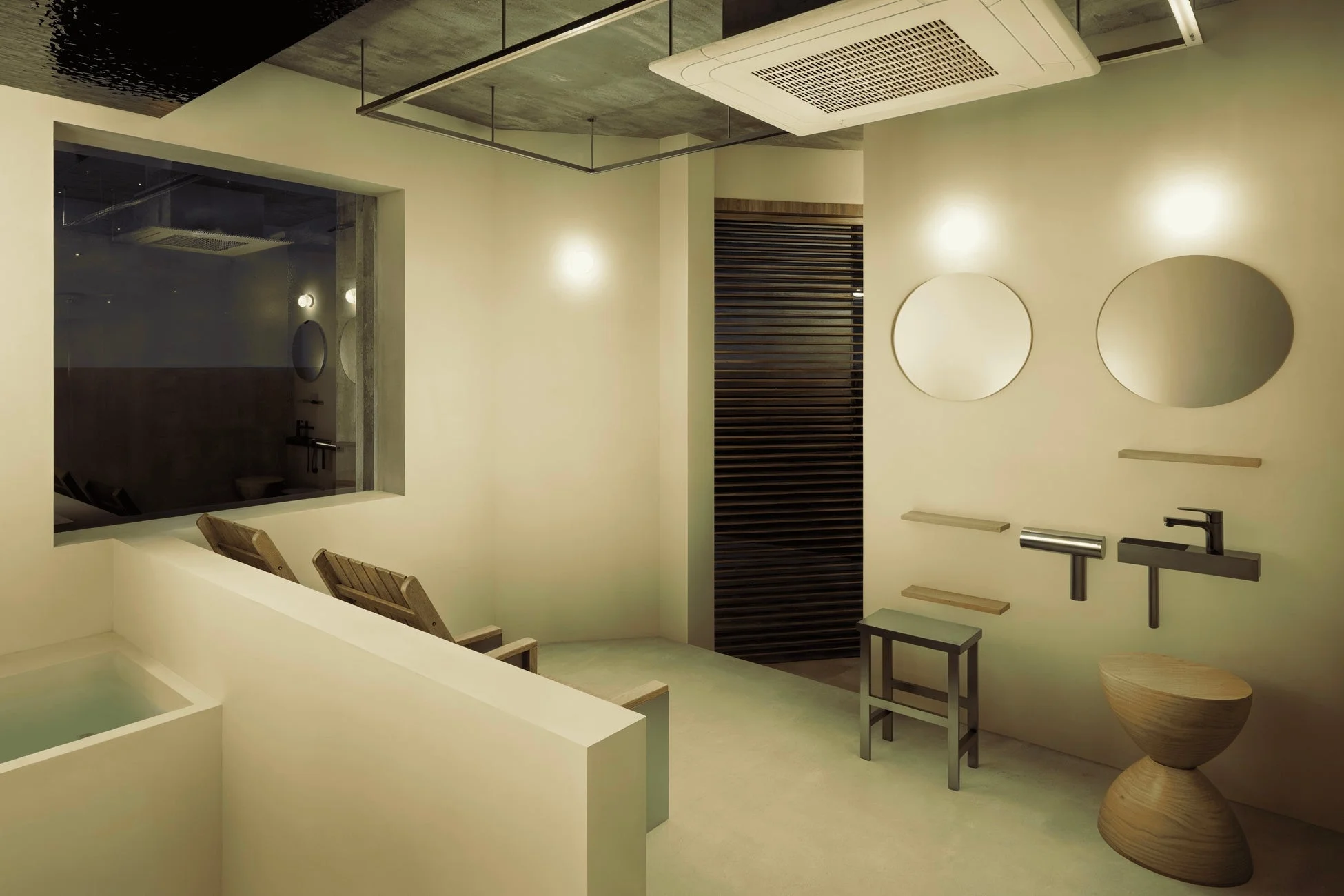 モダンでミニマリストなデザインのバスルームまたはスパ空間です。浴槽とリラックスできる椅子があり、壁には丸い鏡とスタイリッシュな水栓が設置されています。全体的に落ち着いた色調と温かい照明が特徴で、リラックスできる雰囲気を醸し出しています。