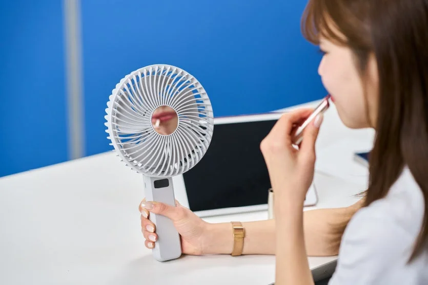 ハンディファンを使いながらリップを塗る女性
